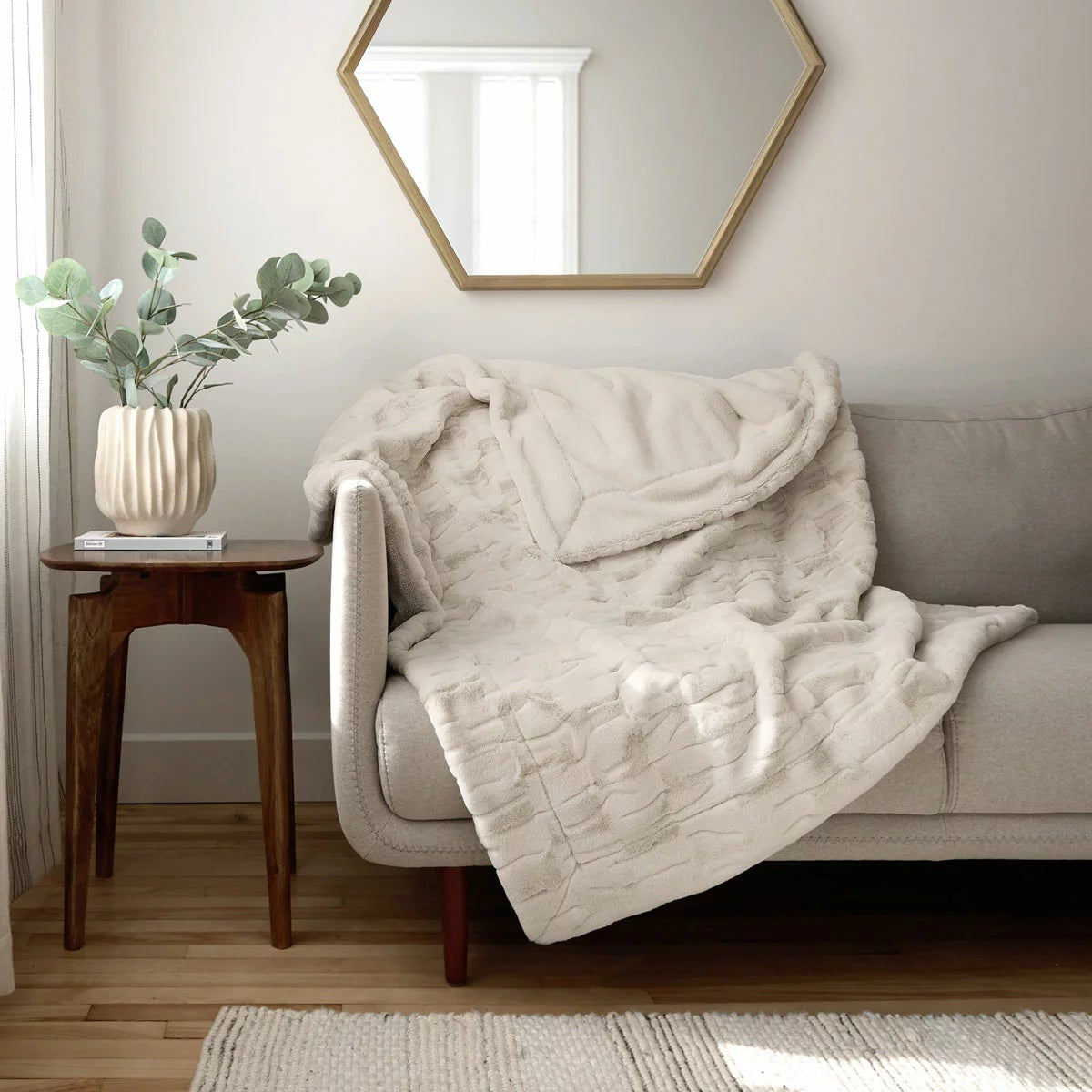 Soft cream Safdie luxury faux rabbit fur throw folded neatly on a grey linen sofa showing off its plush brushed texture.