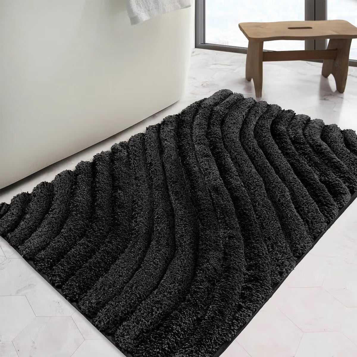 Overhead angled view of the plush grey Safdie Tufted Wave Bath Mat showing its sculpted high-low wave pattern on a light tiled bathroom floor.