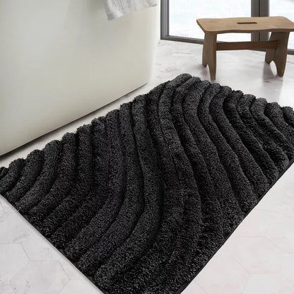 Overhead angled view of the plush grey Safdie Tufted Wave Bath Mat showing its sculpted high-low wave pattern on a light tiled bathroom floor.