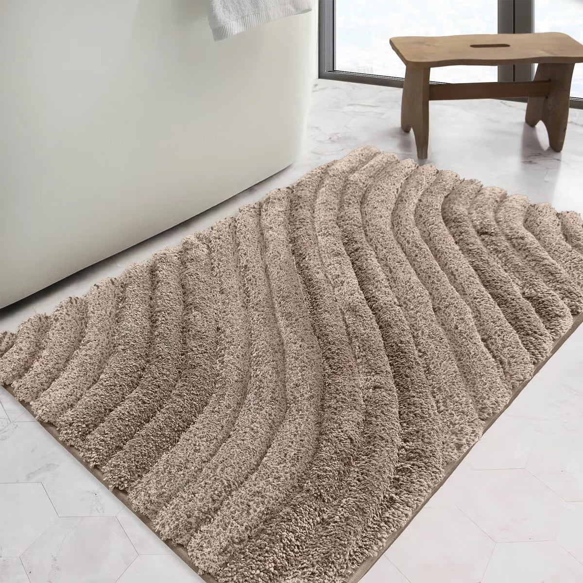 Overhead angled view of the plush grey Safdie Tufted Wave Bath Mat showing its sculpted high-low wave pattern on a light tiled bathroom floor.