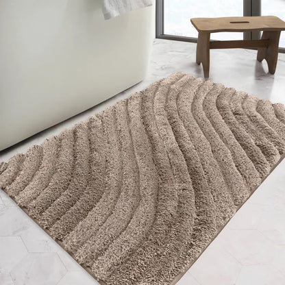 Overhead angled view of the plush grey Safdie Tufted Wave Bath Mat showing its sculpted high-low wave pattern on a light tiled bathroom floor.