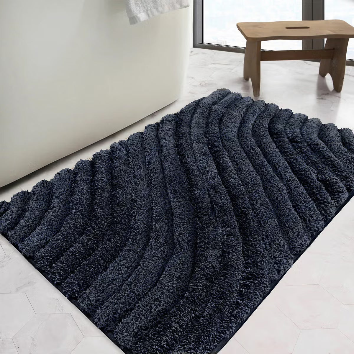 Overhead angled view of the plush grey Safdie Tufted Wave Bath Mat showing its sculpted high-low wave pattern on a light tiled bathroom floor.