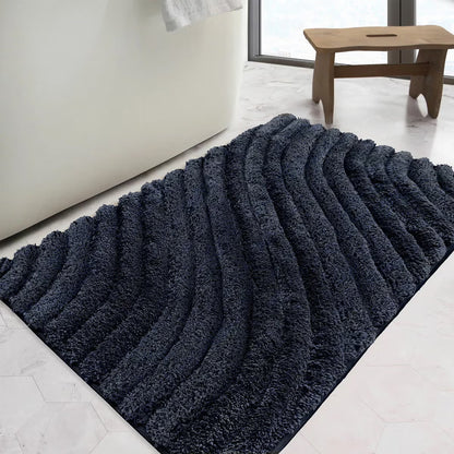 Overhead angled view of the plush grey Safdie Tufted Wave Bath Mat showing its sculpted high-low wave pattern on a light tiled bathroom floor.