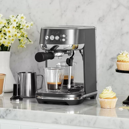 Front view of the compact Sage Bambino Plus espresso machine in sleek matte black stainless steel set on a modern kitchen countertop next to a filled milk jug.