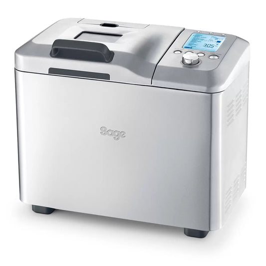 Stainless steel Sage Custom Loaf Pro breadmaker BBM800BSS sitting on a modern kitchen counter with a freshly sliced loaf of golden bread beside it.