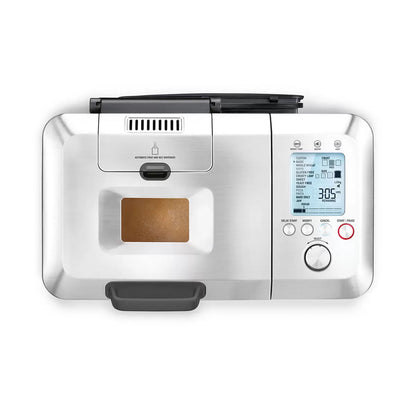 Stainless steel Sage Custom Loaf Pro breadmaker BBM800BSS sitting on a modern kitchen counter with a freshly sliced loaf of golden bread beside it.