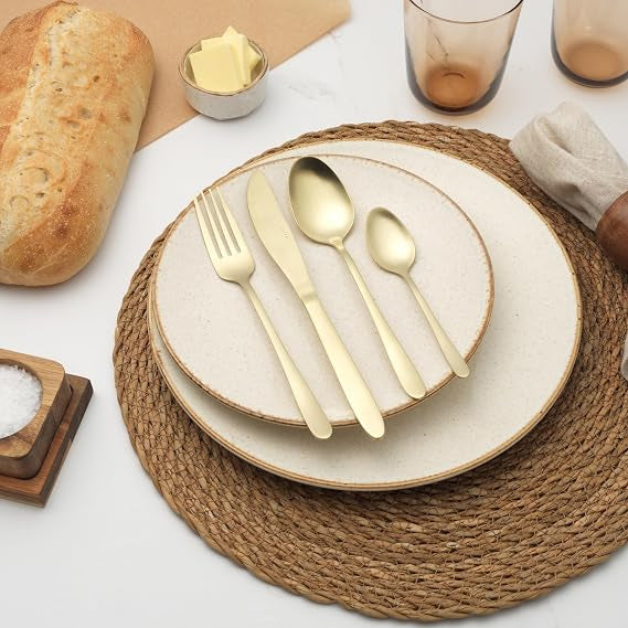 Salter Chiltern 16-piece brushed gold stainless steel cutlery set arranged on a modern dark wood dining table setup.
