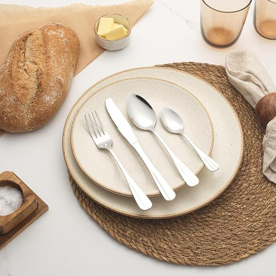 Silver Salter Newbury 16-piece mirror polished stainless steel cutlery set neatly arranged on a wooden dining table including knives, forks, tablespoons, and teaspoons.