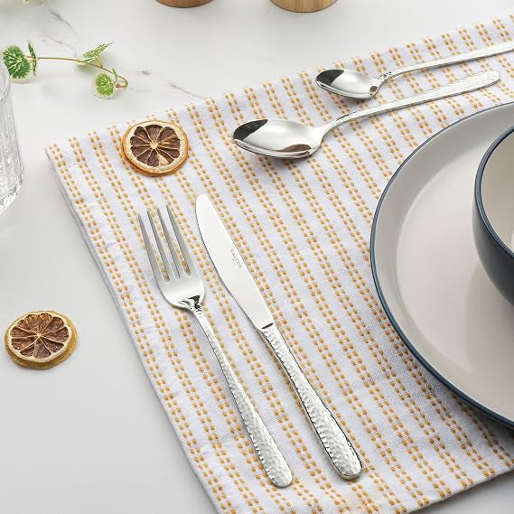 Top-down view of the 16-piece silver Salter Soho cutlery set arranged neatly on a grey linen tablecloth featuring polished knives, forks, tablespoons, and teaspoons.