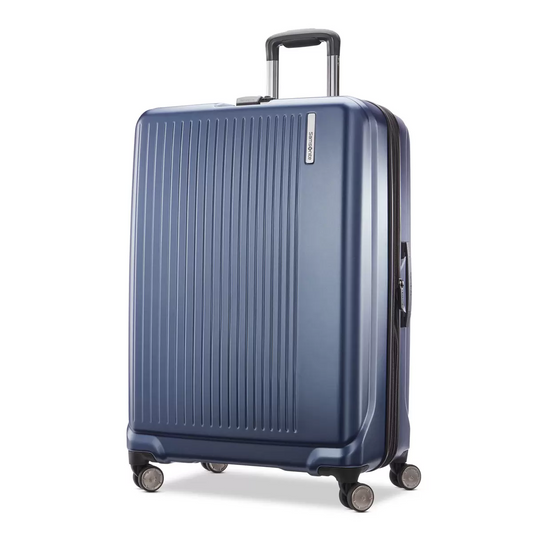 Samsonite Amplitude large hardside case in metallic finish standing upright in a sleek airport terminal corridor.