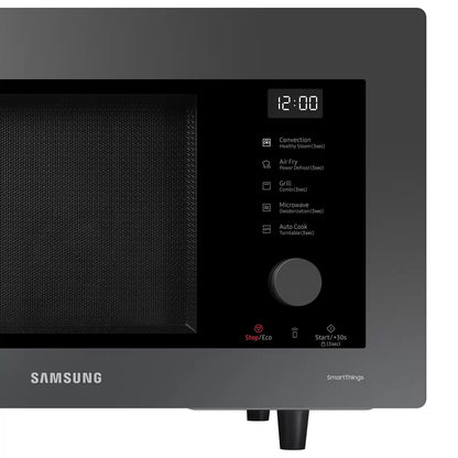 Black Samsung 32L smart microwave oven with glass door and digital control panel sitting on a contemporary kitchen countertop beside cooked food.