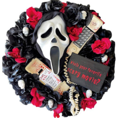 Front view of a round Halloween door wreath featuring a terrifying screaming ghost figure with draped black fabric robes hanging on a dark wooden front door.