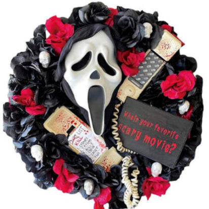 Front view of a round Halloween door wreath featuring a terrifying screaming ghost figure with draped black fabric robes hanging on a dark wooden front door.