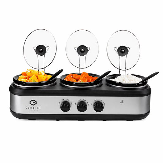 Front angle view of the brushed stainless steel SensioHome Gourmet Triple Slow Cooker 7.1L with glass lids resting on top brackets and serving spoons in place.