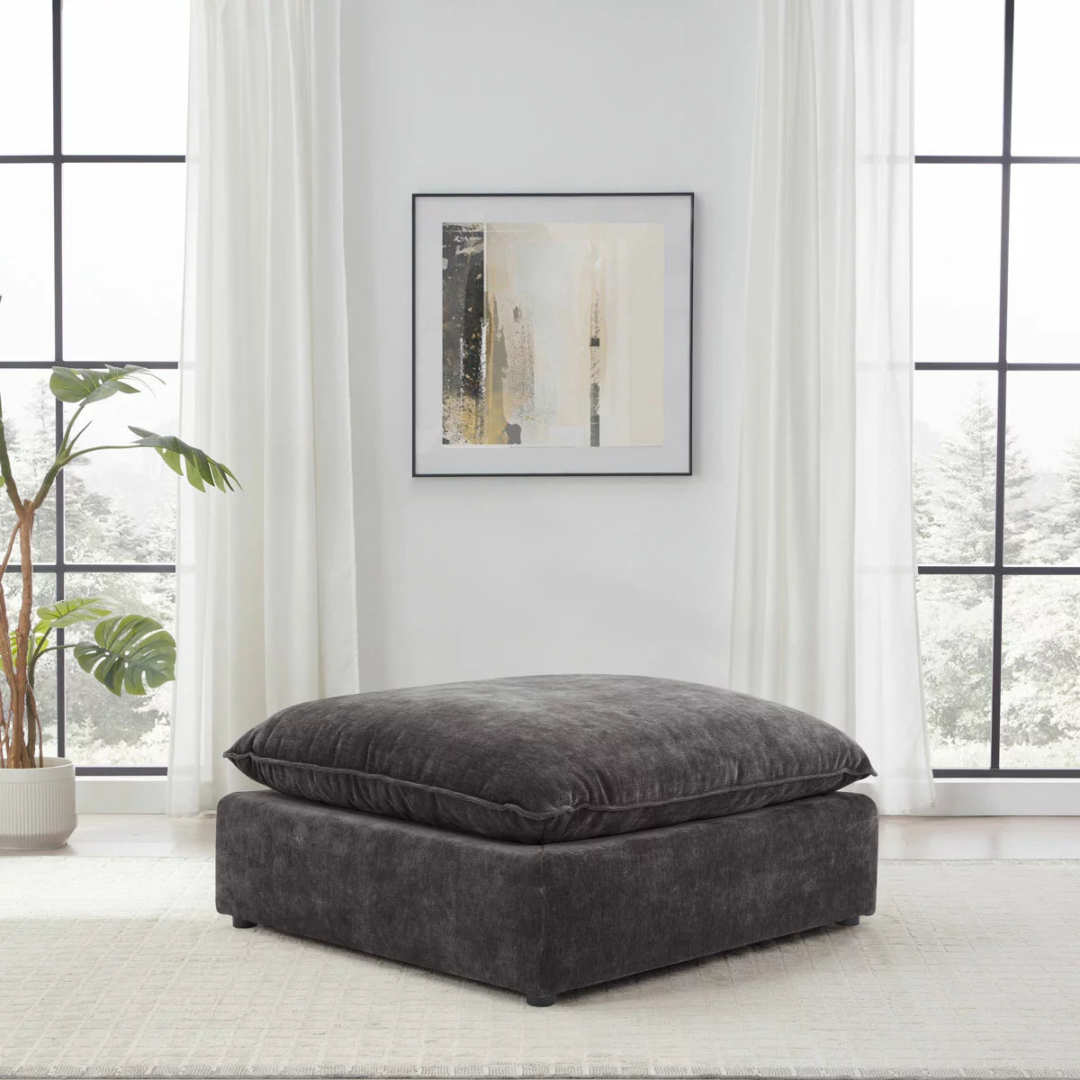 Angled studio shot of the square Sereen dark grey fabric ottoman, showcasing its thick, plush feather-blend cushion top and solid profile on a neutral background.