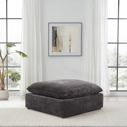 Angled studio shot of the square Sereen dark grey fabric ottoman, showcasing its thick, plush feather-blend cushion top and solid profile on a neutral background.