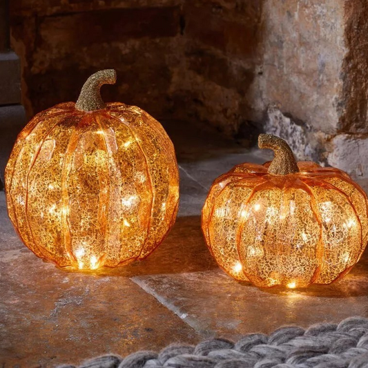 A set of two light-up LED pumpkin ornaments in different sizes glowing warmly on a dark rustic wooden autumn table.