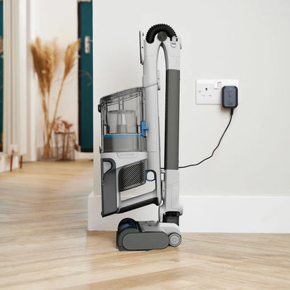 Front angle view of the dark grey Shark PowerPro Pet Cordless Vacuum standing upright on a light wooden floor beside a rug with pet hair accessories attached.