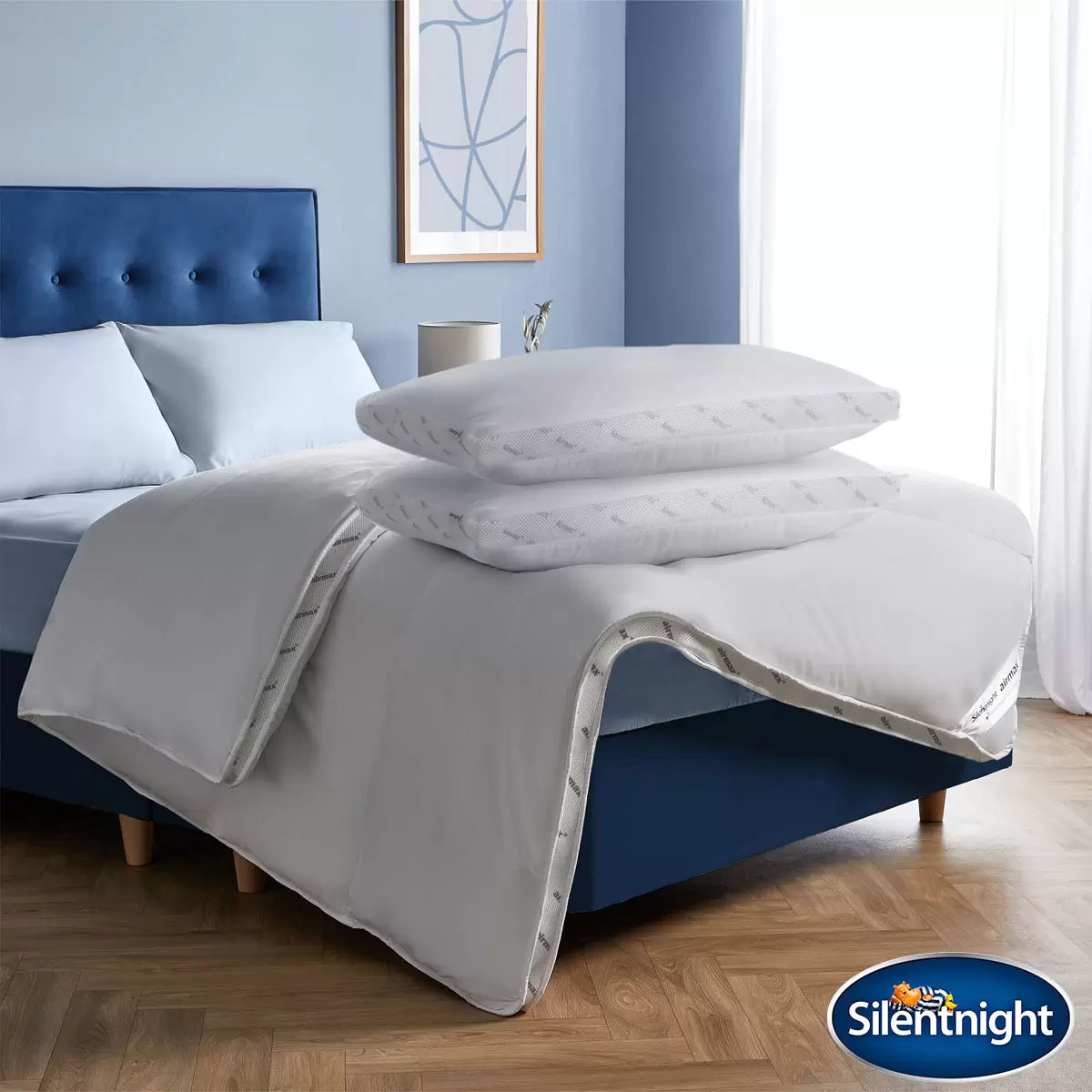 Crisp white Silentnight Airmax 10.5 Tog duvet and two matching pillows with blue mesh side borders arranged neatly on a freshly dressed bed.