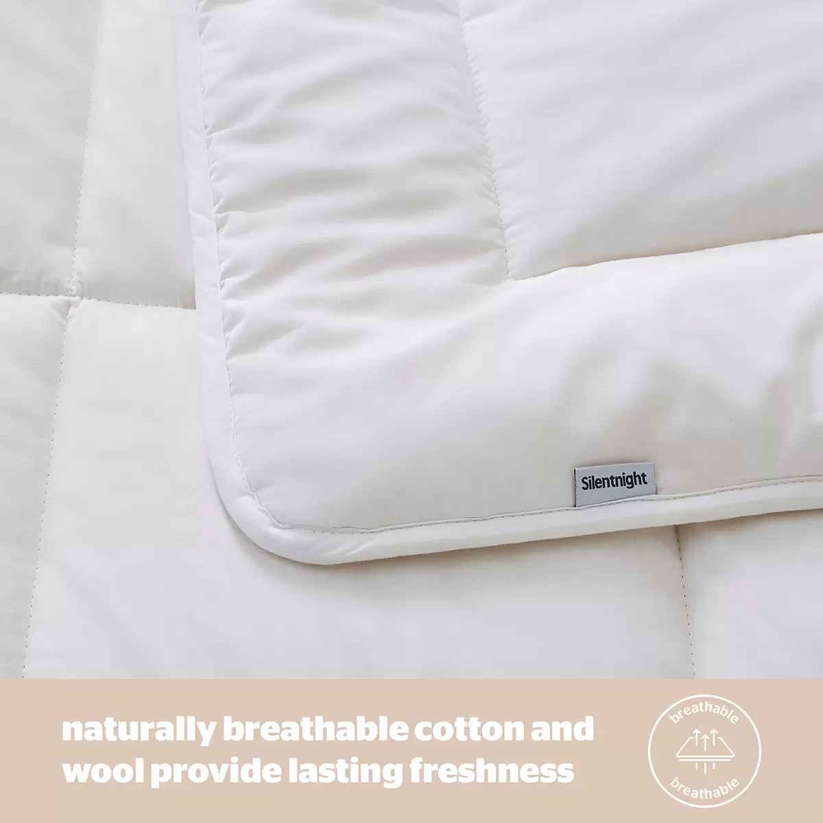Angle view of a thick white Silentnight natural wool heavyweight duvet draped over a modern wooden bed frame in a cozy bedroom setting.