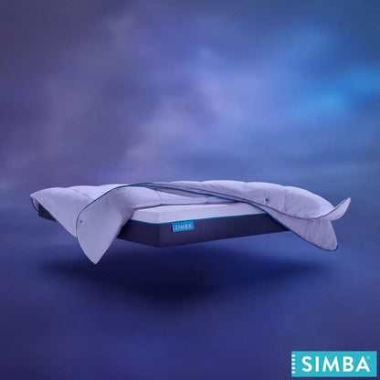 Angle view of the white Simba Hybrid 3-in-1 duvet showing its square-stitched baffle design and snap fasteners dressed neatly on a king-size bed in a sunlit bedroom.