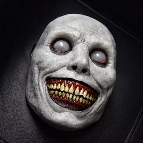 Front view of a creepy ashen gray smiling demon latex mask featuring oversized eyes and a wide gaping mouth.