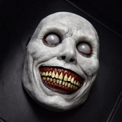 Front view of a creepy ashen gray smiling demon latex mask featuring oversized eyes and a wide gaping mouth.