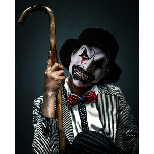 Front view of a creepy half-face smiling evil clown mask featuring painted details, attached dark synthetic hair, and an elastic strap on a clean backdrop.