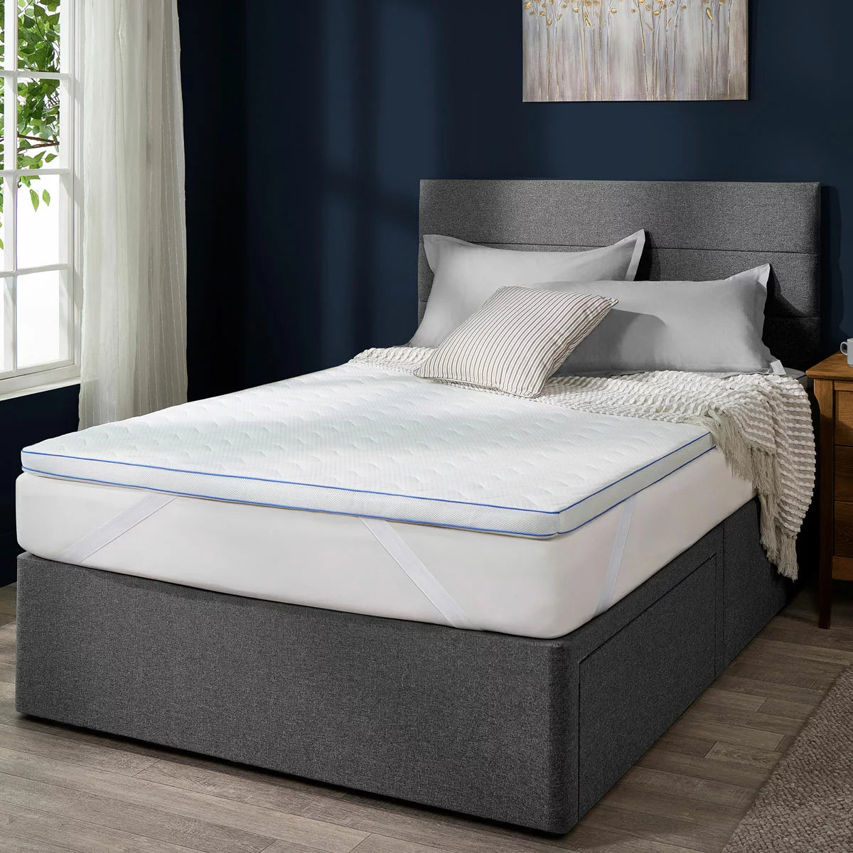 Top-down view of the white Snuggledown King size gel mattress topper on a cozy wooden bed frame, showing the blue Niva cooling gel layer under a breathable mesh-sided polyester cover.