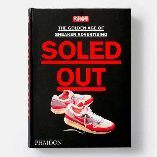 Thick opened hardback copy of Soled Out by Sneaker Freaker showcasing colourful vintage sneaker advertisements on a smooth wooden tabletop.