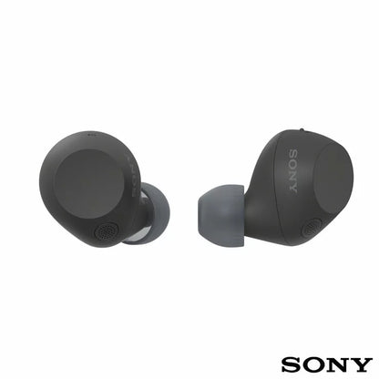 Front angle view of Sony WF-C710N Glass Blue wireless noise cancelling earbuds sitting beside their open charging case on a minimalist wooden desk.