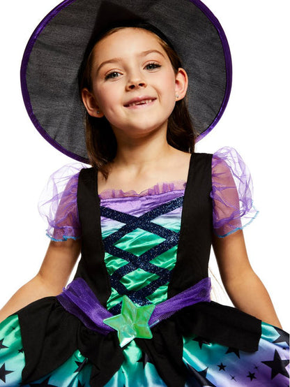 Toddler wearing a purple and black Spell Casting Cutie witch costume with a matching pointed hat outdoors.