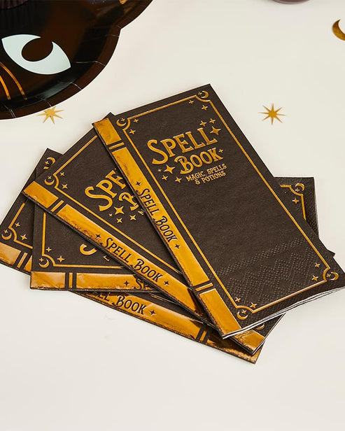 Flat lay view of twelve Spell Yeah! ancient spellbook-themed folded paper party napkins arranged on a dark wooden party table.