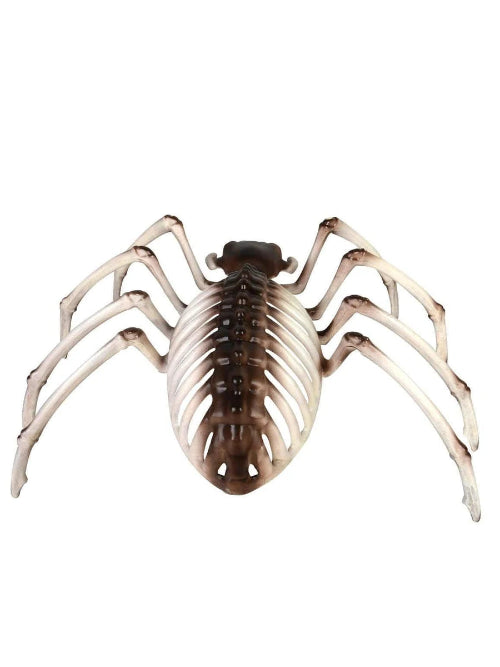 A Smiffys brown and white spider skeleton Halloween prop sitting on a dark wooden table, surrounded by artificial cobwebs under dim atmospheric lighting.