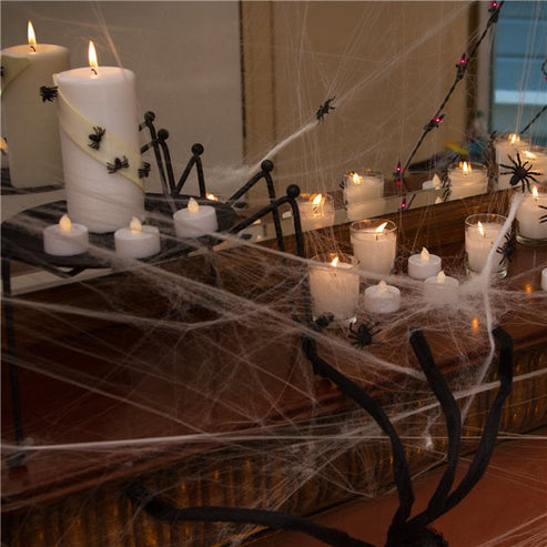White stretchable synthetic spider web draped across a dark wooden doorframe with four small black plastic spiders embedded in the strands.