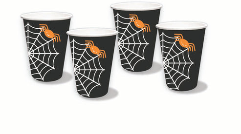 Stacked black and white spider web paper party cups set on a wooden table alongside Halloween party decorations.