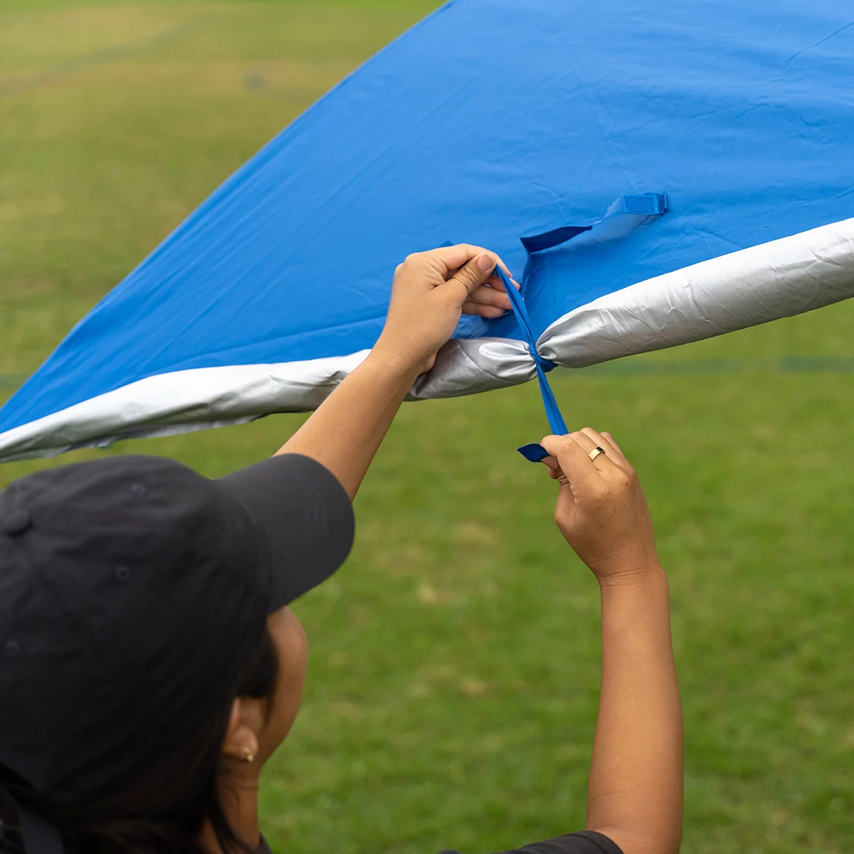Large blue Sport-Brella Ultra 8 foot sun shelter with side privacy panels and built-in wind vents pitched on a sandy beach with lawn chairs underneath.