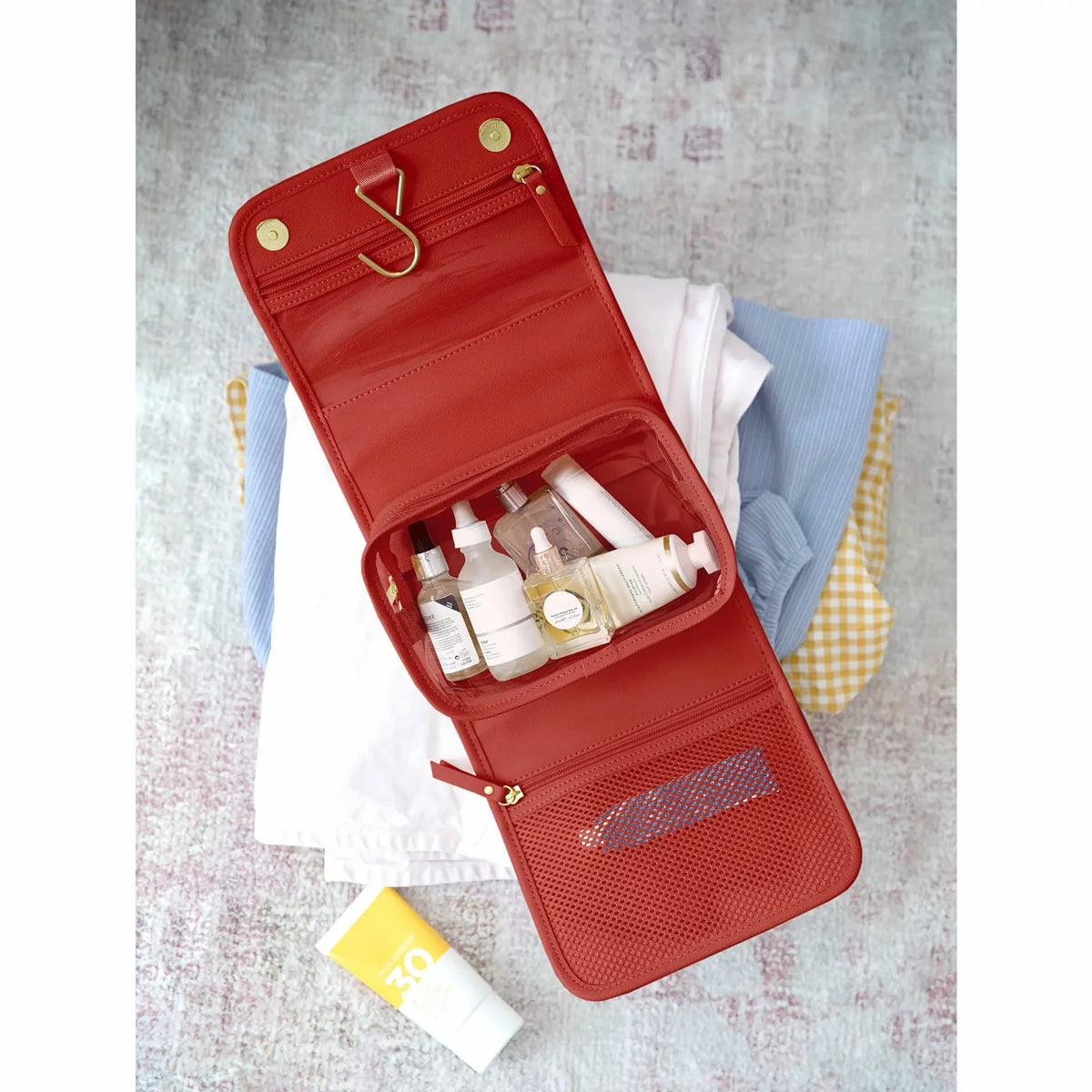Vibrant red Stackers Small Hanging Washbag shown in an open, hanging position on a bathroom hook, showcasing the internal zipped compartments and clear pouch.