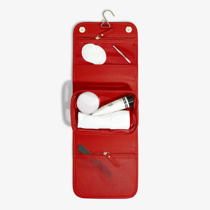 Vibrant red Stackers Small Hanging Washbag shown in an open, hanging position on a bathroom hook, showcasing the internal zipped compartments and clear pouch.