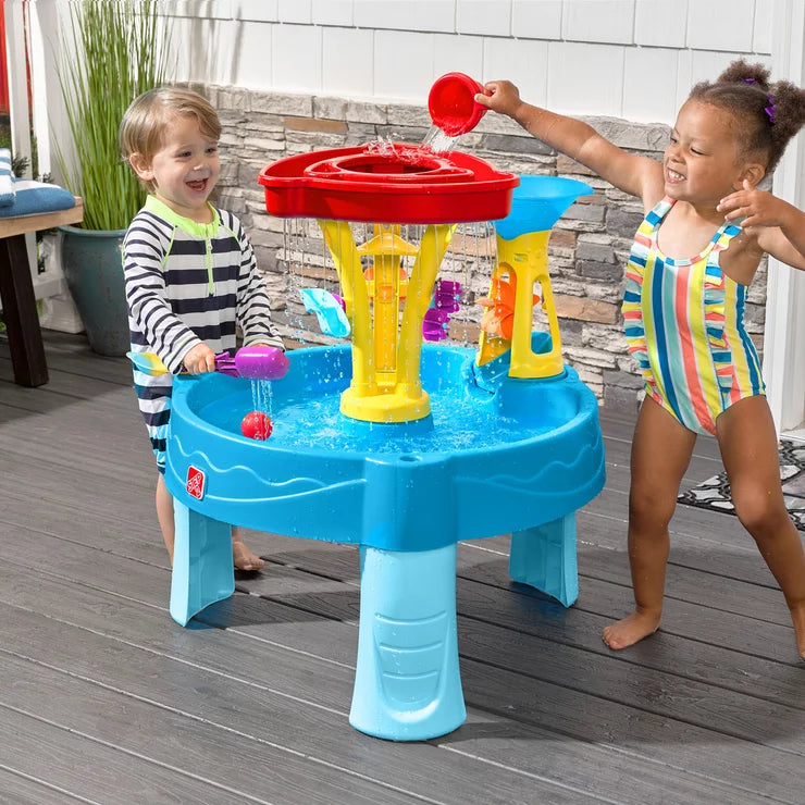 Toddlers playing at a blue and green Step2 Tidal Towers water table with falling water and plastic scoops.