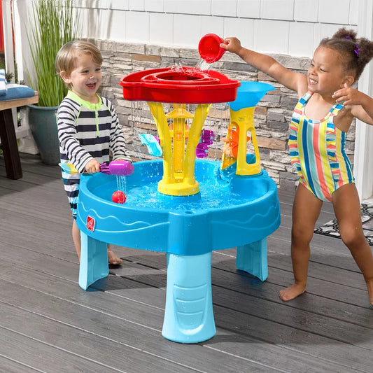 Toddlers playing at a blue and green Step2 Tidal Towers water table with falling water and plastic scoops.