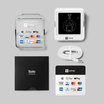 Compact white SumUp Solo touchscreen card reader resting on its angled countertop charging dock displaying a contactless payment prompt.