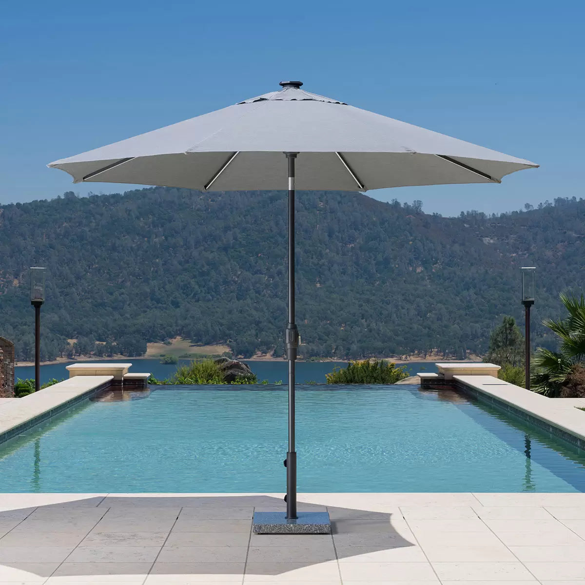 A 10ft grey SunVilla octagonal market umbrella positioned on a wooden deck, showing the dimmable LED rib lighting active in a twilight garden setting.
