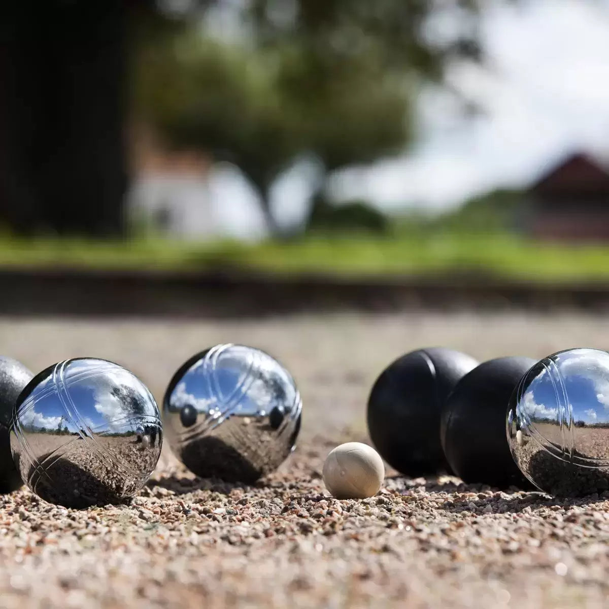 A Sunsport Boules Petanque set featuring six polished and black metal balls, a wooden jack, and a measuring tape arranged neatly next to an open aluminium storage case on a grassy garden lawn.