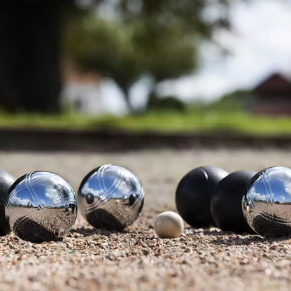 A Sunsport Boules Petanque set featuring six polished and black metal balls, a wooden jack, and a measuring tape arranged neatly next to an open aluminium storage case on a grassy garden lawn.