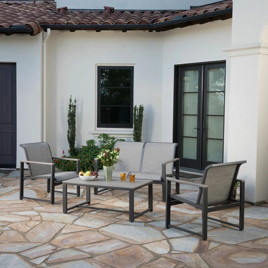 Sunvilla Helio four-piece sling patio set featuring a double loveseat, two armchairs with faux-wood armrests, and a matching coffee table on a tiled garden patio.