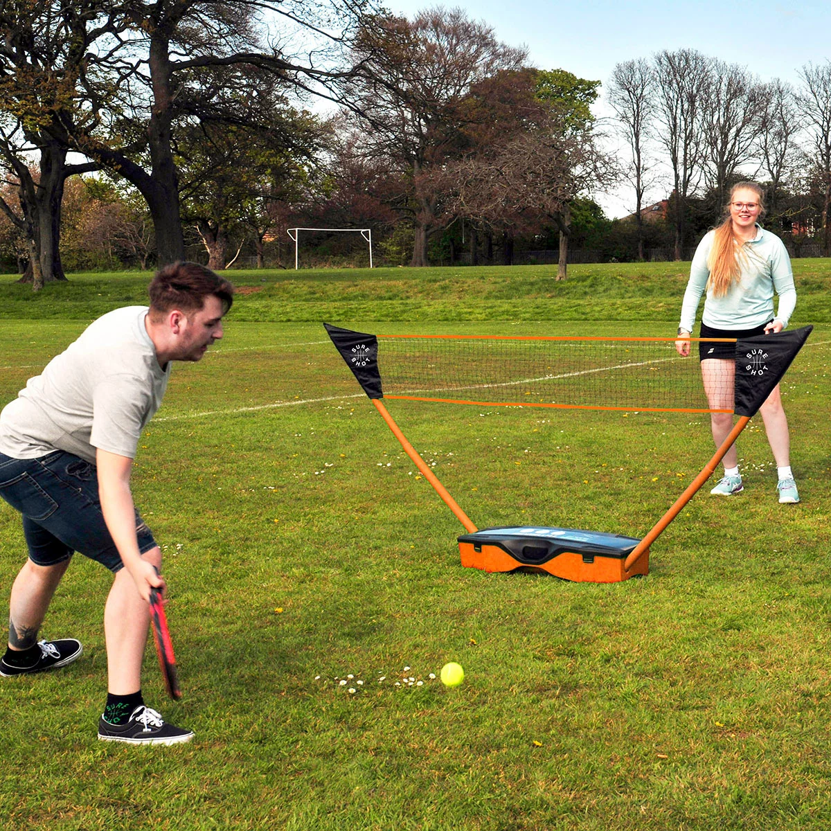 Complete Sure Shot 3-in-1 sports set set up on a green garden lawn showing the adjustable net, tennis rackets, badminton rackets, shuttles, and volleyball neatly laid out beside the blue base trunk.