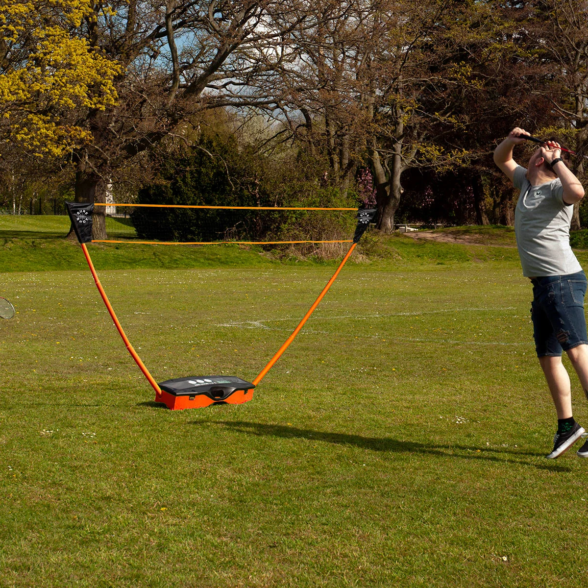 Complete Sure Shot 3-in-1 sports set set up on a green garden lawn showing the adjustable net, tennis rackets, badminton rackets, shuttles, and volleyball neatly laid out beside the blue base trunk.