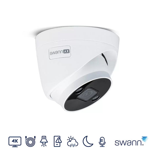 White Swann 4K dome security camera with built-in spotlights and clear glass casing mounted against a dark exterior wall.