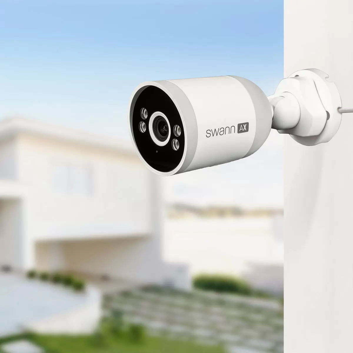 Profile view of the white and black Swann 4K bullet security camera mounted to a brick wall, showcasing its integrated LED spotlight, microphone port, and compact housing in an outdoor residential environment.